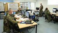 Soldatinnen und Soldaten sitzen an Bildschirmarbeitsplätzen. Im Hintergrund stehen Wände mit verschiedenen Karten.