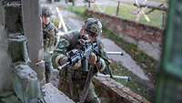 Ein Soldat schaut mit seinem Gewehr G36 im Anschlag durch ein Fenster