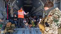 Viele Menschen sitzen dicht an dicht im Laderaum eines Flugzeugs.