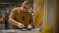 Ein Soldat hält eine Briefmarke in der Hand und klebt diese, auf eine Karte