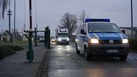 Ein Polizeiauto fährt vor einem LKW auf einer Straße durch eine Toreinfahrt.