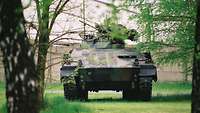 Ein Panzer steht zwischen Bäumen auf einer Wiese.