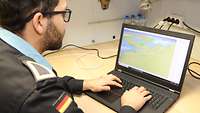 Ein Soldat arbeitet an einem Laptop, auf dem eine Seekarte zu sehen ist
