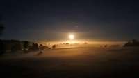 Über einer Landschaft in der Nacht steht über dem Horizont ein runder Feuerball.