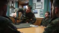 Soldaten sitzen an einem Tisch. Darauf steht ein Maschinengewehr, das ein Soldat auseinandernimmt. 