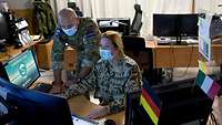 Eine Soldatin sitzt am Schreibtisch und ein weiterer niederländischer Soldat steht daneben. Beide gucken in Computerbildschirme