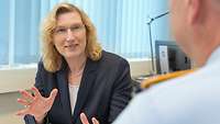 Man sieht die Präsidentin über die Schulter des Interviewers, sie blickt diesen an und macht dabei eine gestaltende Geste.