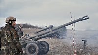 Mehrere Soldaten stehen mit einer Feldhaubitze auf nebligem Übungsgelände und schießen.