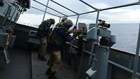 Drei Soldaten stehen an Maschinengewehren an Deck eines Schiffes