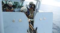 Drei Soldaten stehen hinter einem Maschinengewehr, einer hält ein Fernglas in den Händen