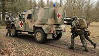 Zwei Soldaten schieben einen Verwundeten auf einer Trage in ein Militärfahrzeug mit Sanitätskreuz.