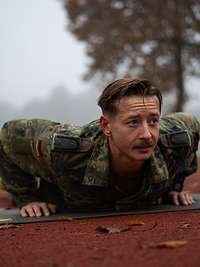 Training für einen Wettkampf an der Universität der Bundeswehr Ein Soldat liegt draußen auf rotem Tartanboden und macht Liegestütze.