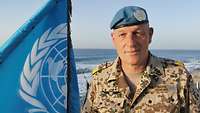 Flottillenadmiral Andreas Mügge Ein Soldat steht neben einer UN Fahne