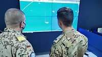 Zwei Soldaten verschiedener Nationen schauen auf eine Leinwand