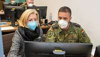 Eine Frau und ein Soldat betrachten gemeinsam den Bildschirm eines PC.