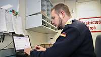 Ein Marinesoldat in einem dunkelblauen Pullover sitzt vor einem Laptop.