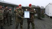 Zwei Soldaten stehen auf einem Platz vor der Truppe und halten eine Zertifizierungsurkunde in den Händen.