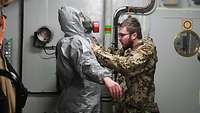 Ein Soldat hilft einem weiteren Soldaten in die Schutzkleidung