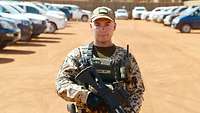 Ein Soldat steht in einem Camp. Im Hintergrund stehen mehrere Fahrzeuge.