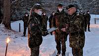 Vor einer Formation Soldaten überreicht im Schnee ein Soldat eine Auszeichnung an eine Soldatin.