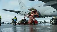Flughafenpersonal in gelben Warnwesten arbeitet bei der Gepäckentladung am Flugzeugheck