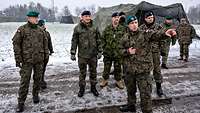 Auf einer verschneiten Wiese stehen mehrere Soldaten vor grünen Zelten.