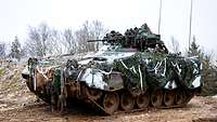 Schützenpanzer von schräg vorn mit Tarnnetzen abgehangen