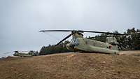 Zwei sehr große Hubschrauber mit Doppelrotoren stehen an einem leichten Hang.