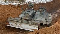 In einem tiefen Panzergraben arbeiten Soldaten mit ihrem Panzer.