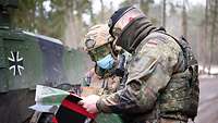 Ein belgischer und ein deutscher Soldat besprechen sich mit Blick auf eine Karte. Hinter ihnen steht ein Panzerspähwagen.