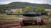 Ein Kampfpanzer Leopard 2 A7V fährt im Gelände. Zwei Soldaten schauen aus den Luken des Fahrzeuges.