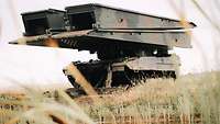 Ein Brückenlegepanzer Leguan steht auf einer Wiese vor einem Gewässer