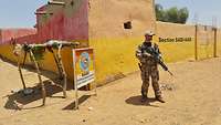 Ein Soldat steht mit einer Waffe vor einer Wand und beobachtet die Umgebung 