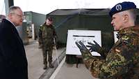Ein Zivilist und ein Soldat unterhalten sich, im Hintergrund ein weiterer Soldat an einem Plakat