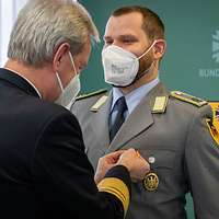 Ein Soldat befestigt einen Ehrenkreuz an der Uniform eines Soldaten