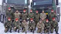 Gruppenbild von 14 Soldaten vor zwei Militärfahrzeugen