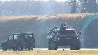 Ein Transportpanzer Fuchs und ein Geländewagen stehen vor einem Flugzeugshelter.