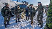 In verschneitem Gelände laufen und stehen mehrere Soldaten, im Hintergrund ein Gefechtsfahrzeug.