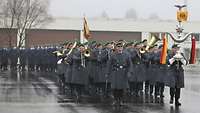 Soldaten des Heeresmusikkorps marschieren in grauen Uniformen über den Appellplatz und musizieren.