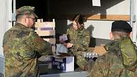 Eine Soldatin sitzt im Laderaum eines Lkws und packt Verpflegungsbeutel. Zwei Soldaten schauen zu