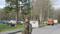 Ein Soldat steht auf einer Straße und hebt eine Winkerkelle in die Höhe.