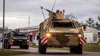 Mehrere Transportpanzer rollen durch ein Kasernentor.
