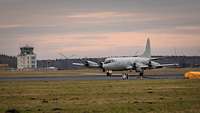 Ein hellgraues, viermotoriges Propellerflugzeug auf einem Flugplatz.