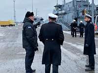Minenjagdboote Tallinn Marinesoldaten in dunkelblauen Uniformmänteln stehen auf einer Hafenpier; im HIntergrund zwei kleine, graue Kriegsschiffe.