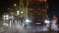 Männer in weißen Anzügen spritzen einen großen LKW mit Wasser ab.