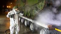 Moldat in weißen Anzug spritzt einen großen LKW mit Wasser ab.