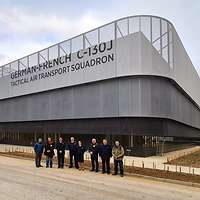 Acht Personen stehen vor einem großen Gebäude auf einem Flughafen