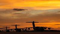 Drei Transportflugzeuge vom Typ A400M stehen in der Dämmerung auf einem Militärflugplatz.