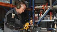 Ein Soldat flext in einer Werkstatt an einem Stück Metall
