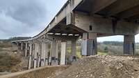 An den Pfeilern einer Betonbrücke sind auf halber Höhe Tücher wie Schürzen angebracht.